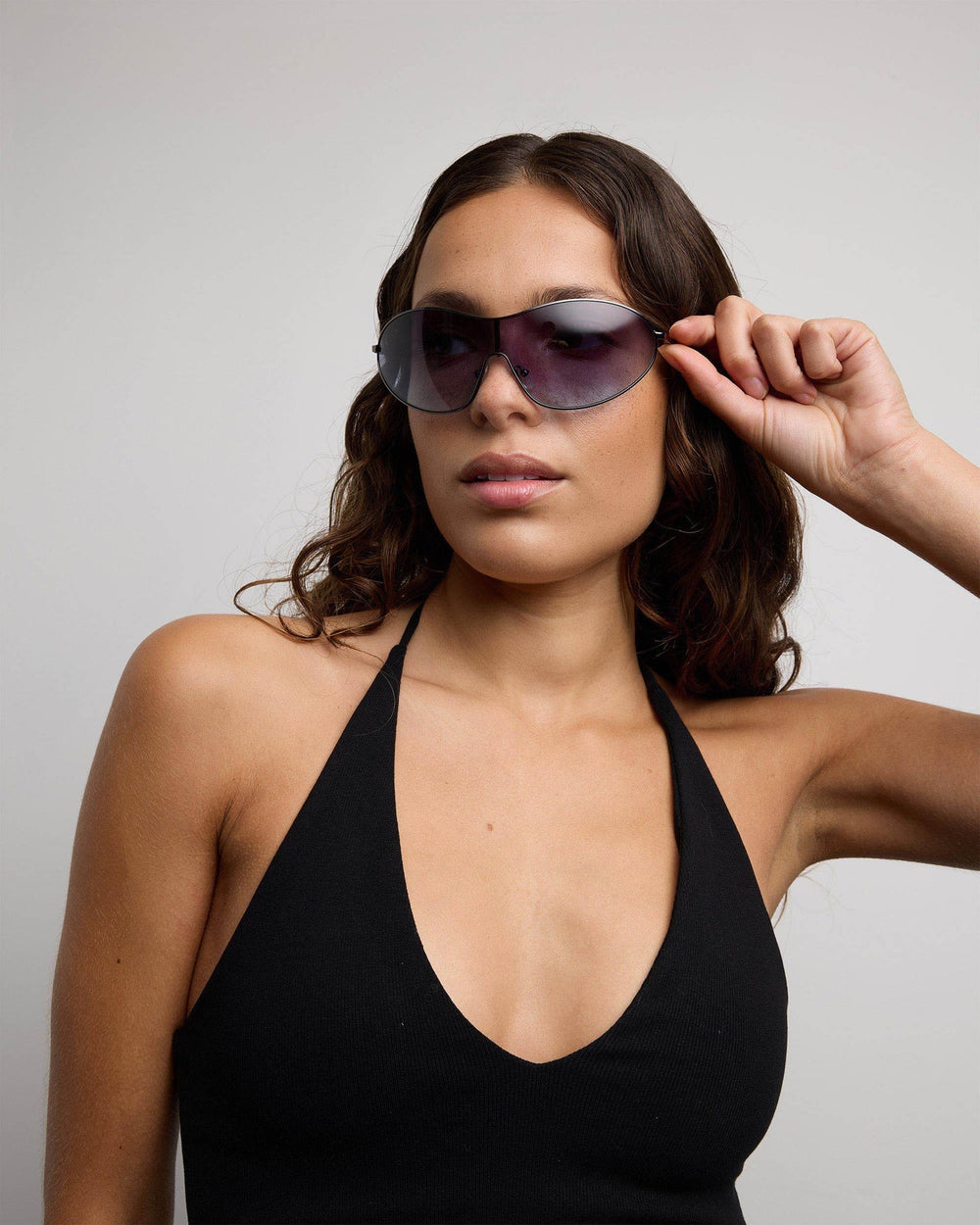 Woman wearing a black halter top and sunglasses against a gray background